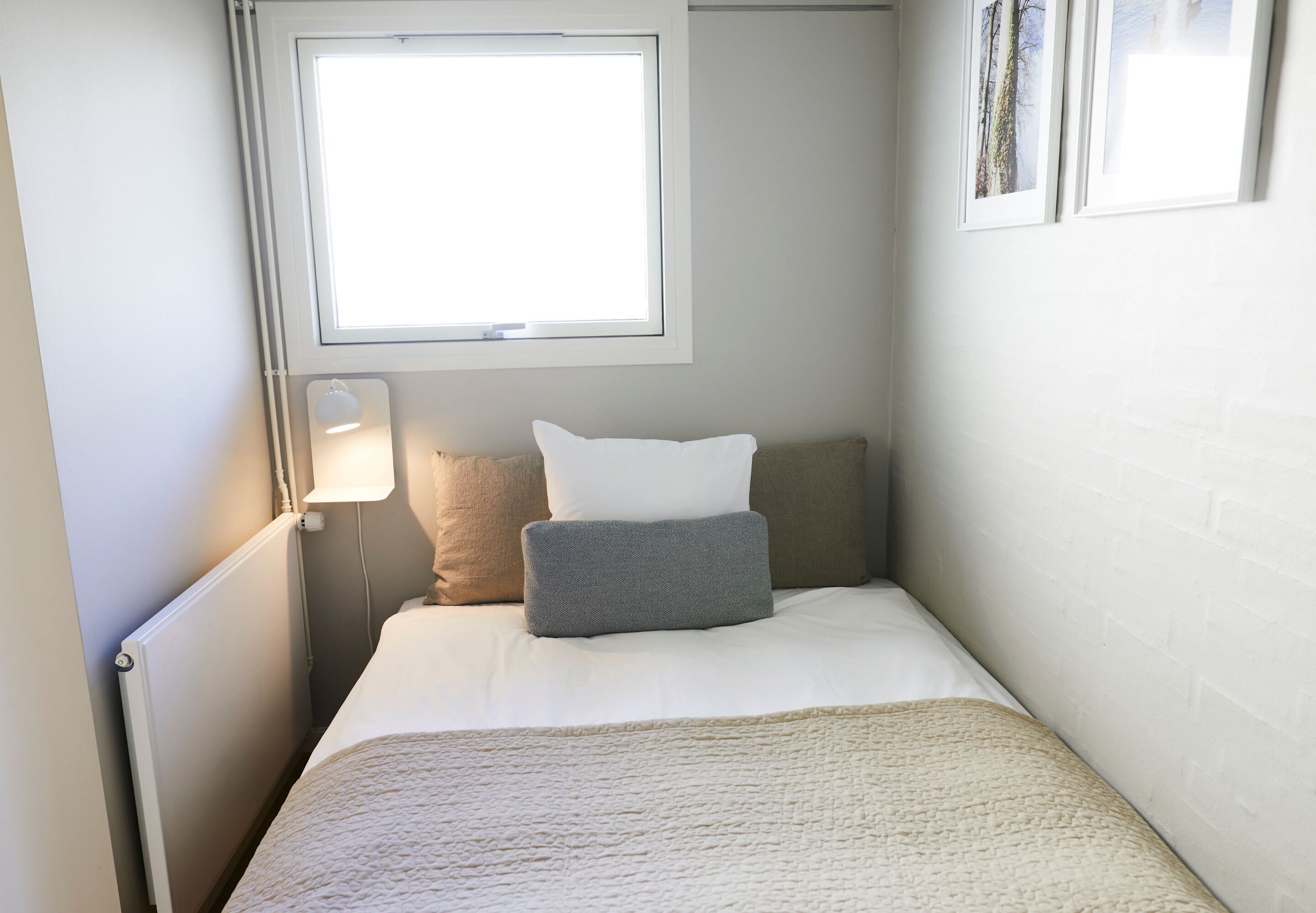 Un dormitorio pequeño y ordenado con una cama individual, una lámpara de noche y un ventanal que proporciona luz natural.