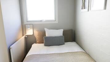 Un dormitorio pequeño y ordenado con una cama individual, una lámpara de noche y un ventanal que proporciona luz natural.