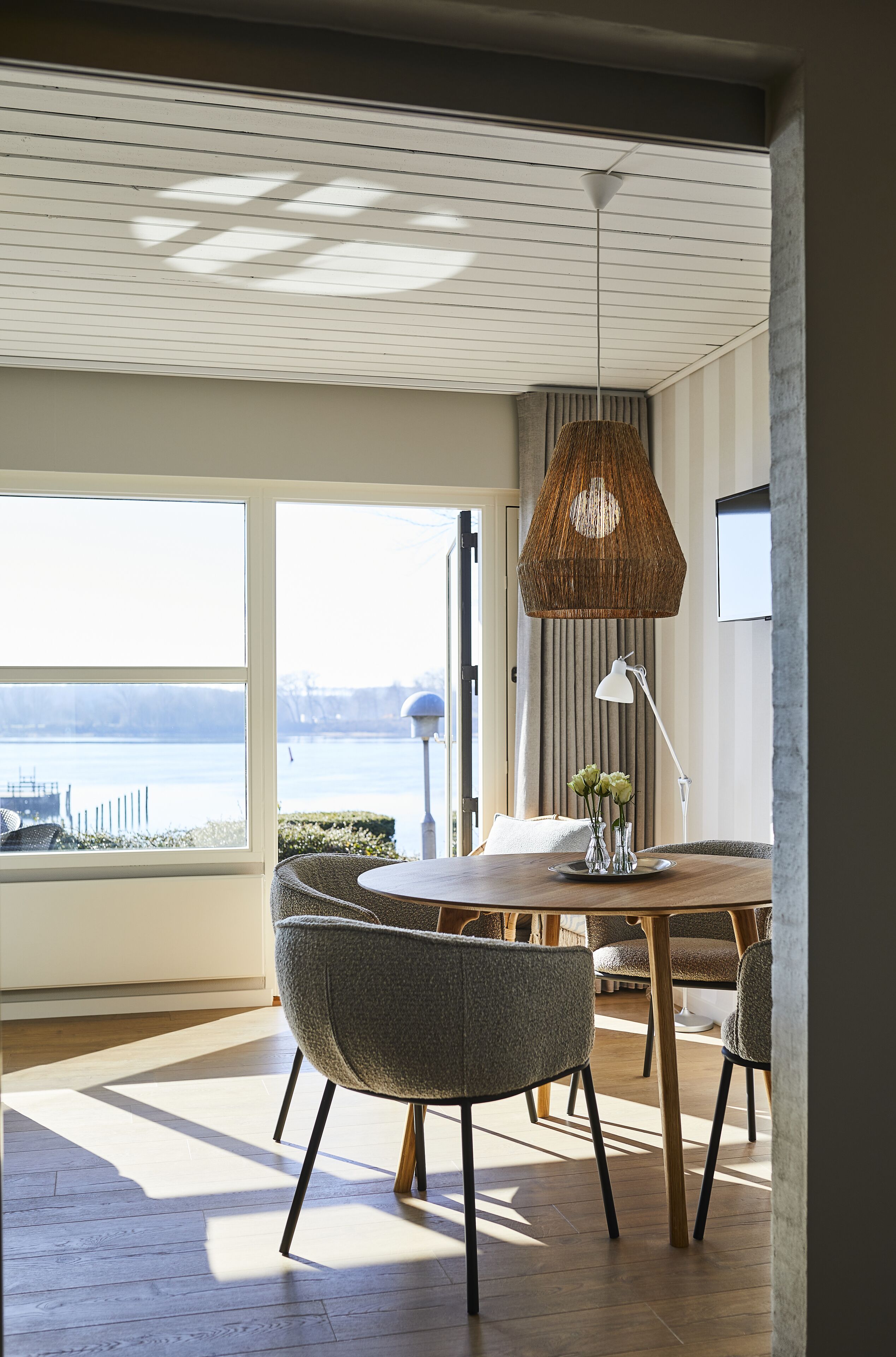 Un área de comedor con vistas a una masa de agua, una lámpara colgante de mimbre y una mesa con sillas.