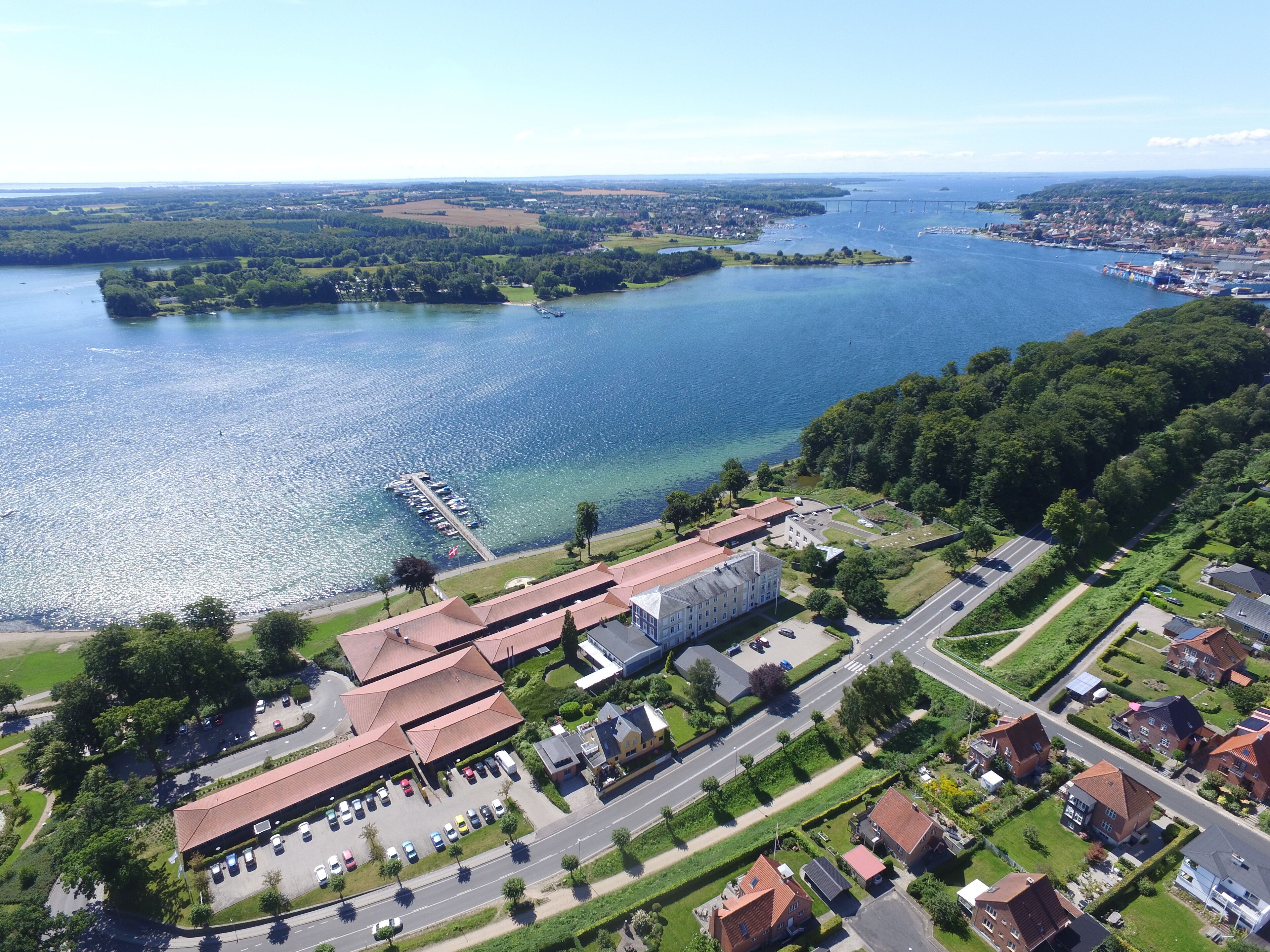 Vista aèria d'una zona costanera amb un port esportiu, un edifici gran amb teulada vermella i cases residencials.