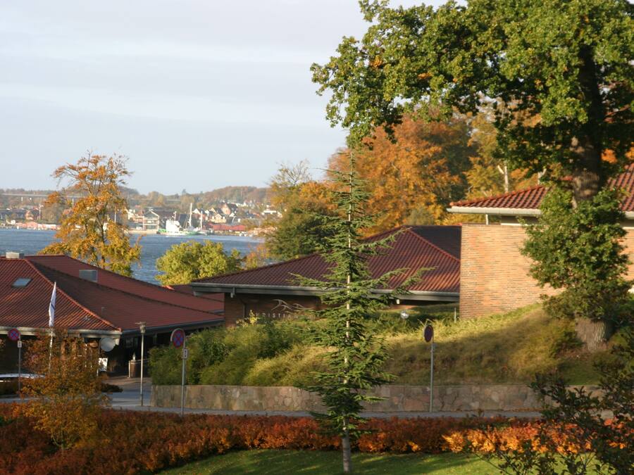 A coastal hotel with a view of the sea, featuring a brick building with a red roof, a covered outdoor area, and a landscaped garden.