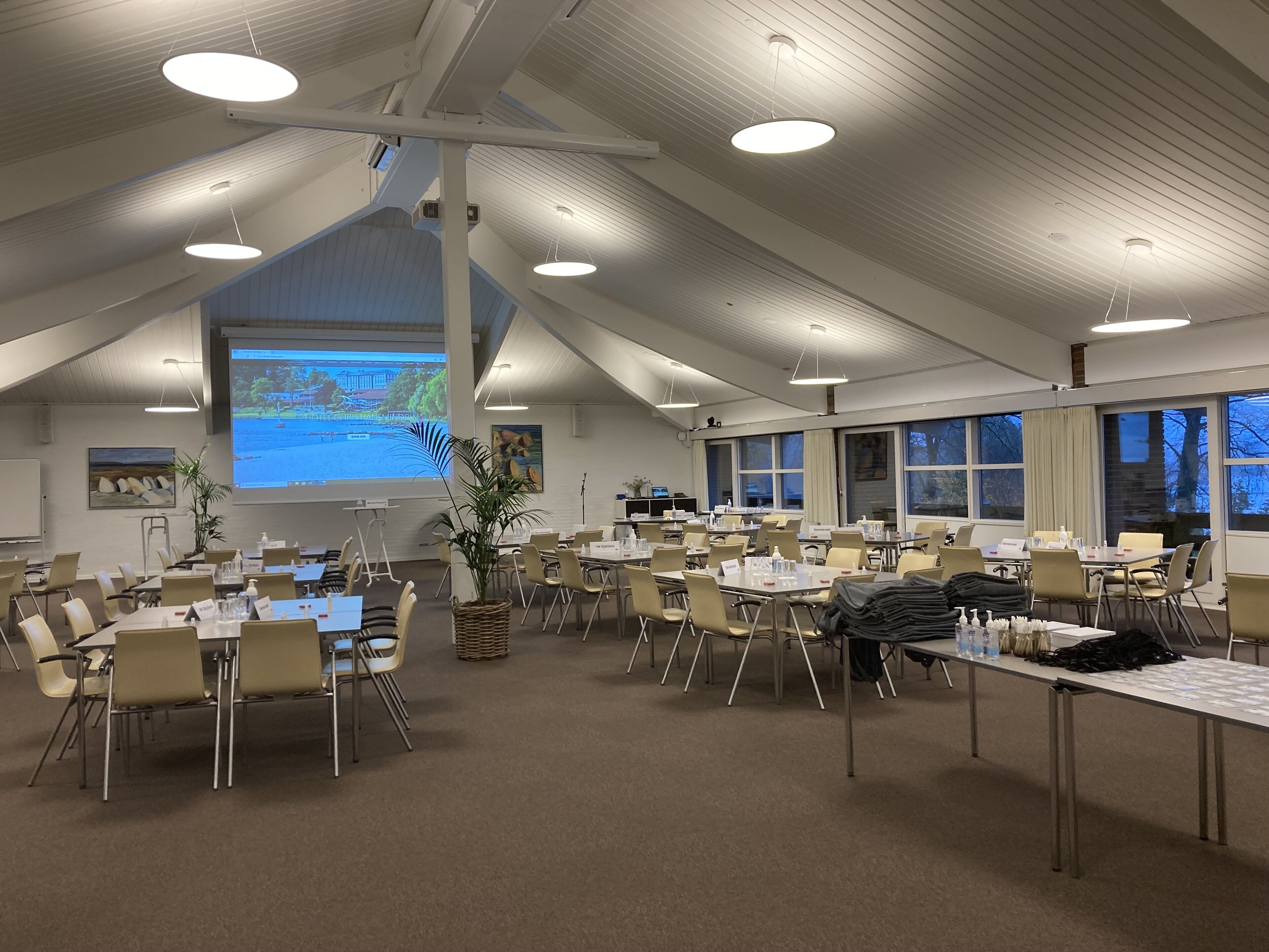 Un salón de conferencias con mesas, sillas, una pantalla de proyector y un ventanal grande.