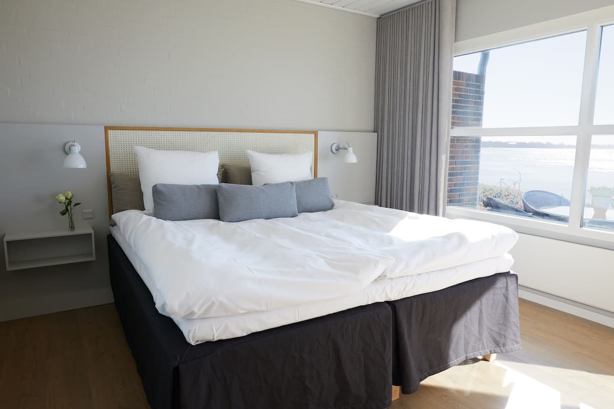 A neatly made bed with white and gray linens, a wooden headboard, and two bedside lamps.