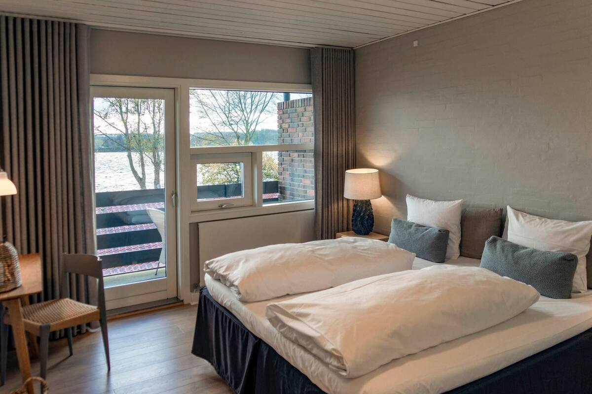 A hotel room with a bed, a desk, and a chair. There is a window with a view of trees and a building.