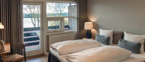A hotel room with a bed, a desk, and a chair. There is a window with a view of trees and a building.