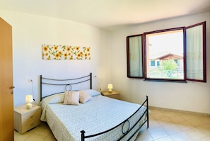 A bedroom with a bed, bedside tables, a wall-mounted lamp, and a window with curtains. - Casa in Maremma Tuscany Village (Scarlino)