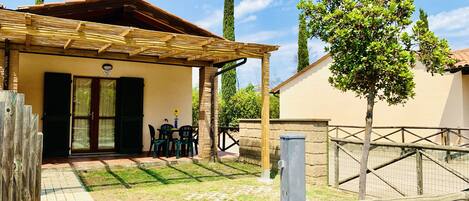 Un espace extérieur abrité, avec une table et des chaises, une porte portant un numéro et un jardin clos.