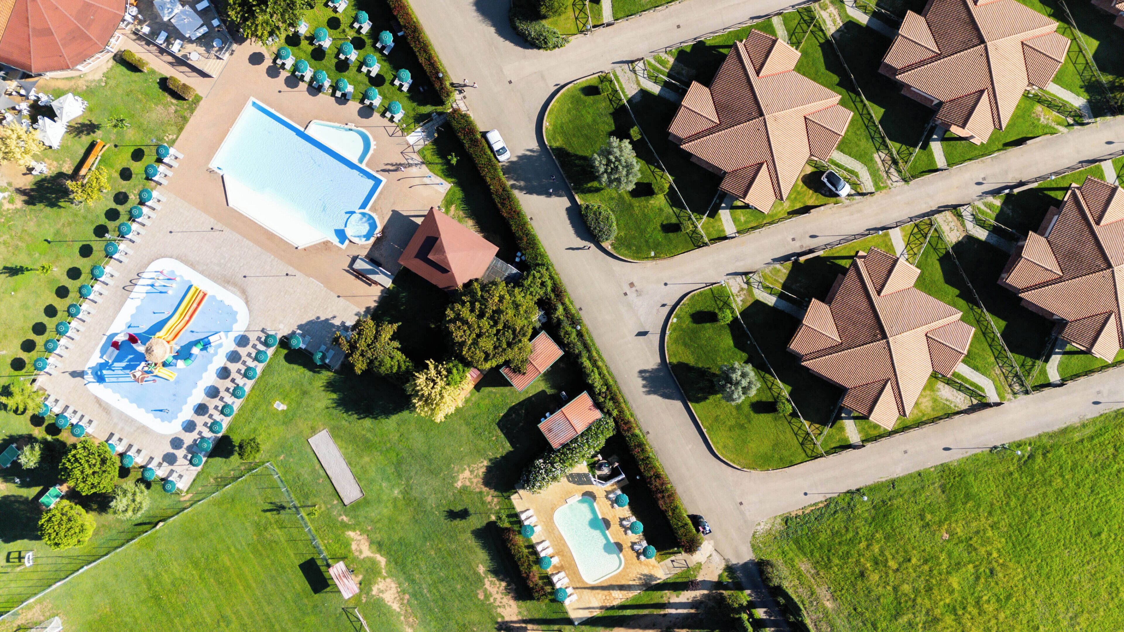 An aerial view of a resort with multiple pools, sun loungers, and a central building with a red roof.