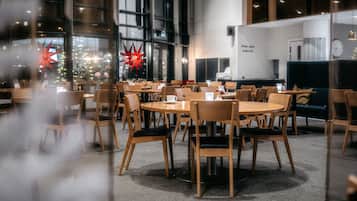 Un amplio comedor interior con mesas redondas y sillas de madera, ventanas grandes con luces rojas con forma de estrella y un diseño de interiores moderno.