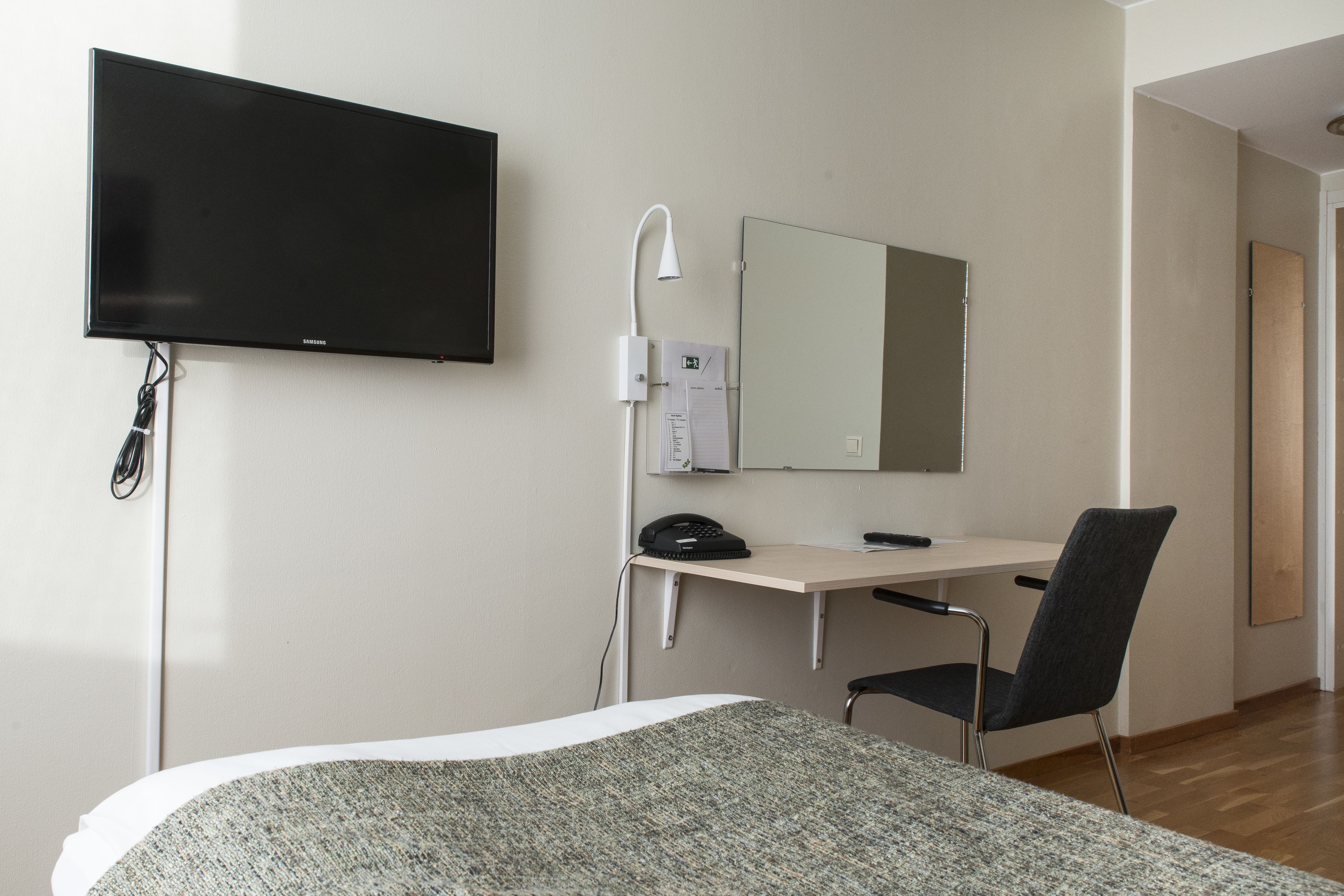 Una camera d'albergo con un letto, una scrivania con una sedia, una TV a schermo piatto, uno specchio e un telefono.