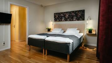 A double bed with a dark headboard, two bedside tables with lamps, a wall-mounted TV, and a wooden floor.