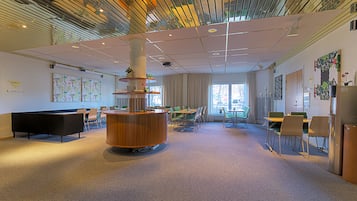 Un moderno vestíbulo de hotel con un mostrador de recepción de madera central, varias zonas de estar y grandes ventanales que proporcionan luz natural.