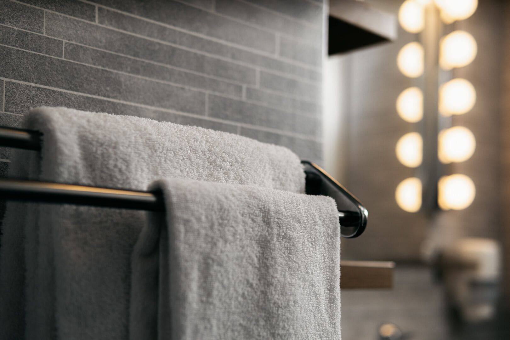 Ein Badezimmer mit Handtuchhalter, zwei Handtüchern, einer Ziegelwand und einer Leuchte mit mehreren Lampen.