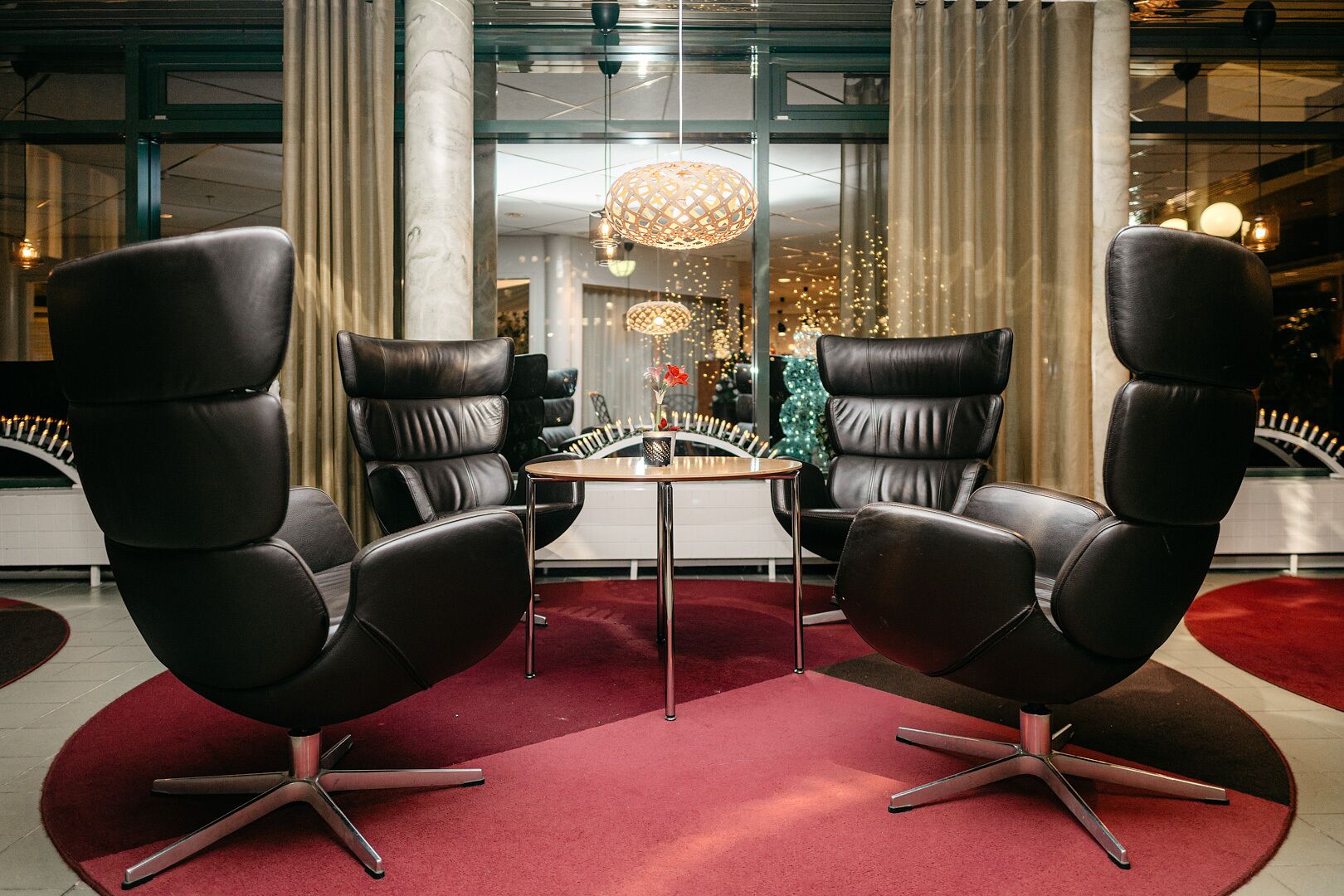 Een moderne kamer met twee zwarte lederen fauteuils, een klein rond tafeltje en een rood tapijt.