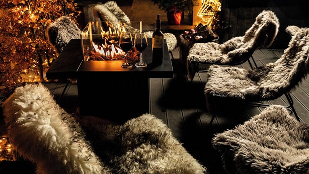 A cozy outdoor seating area with a fire pit, fur-covered chairs, and a Christmas tree. - Design-Hotel JAMS (Munich)