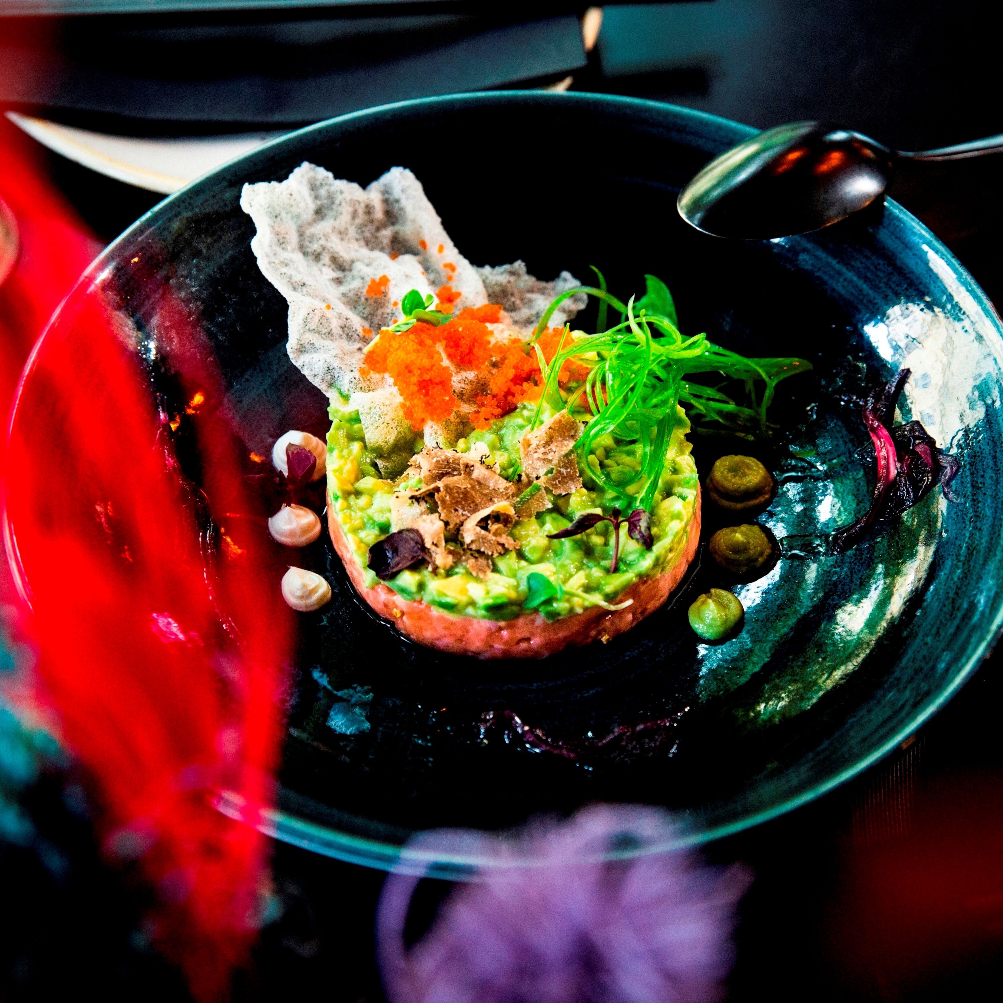 A dish with avocado, greens, and other toppings on a black plate.