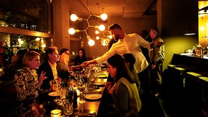 A restaurant interior with tables set for dining, a waiter attending to guests, and a bar area in the background. - Design-Hotel JAMS (Munich)