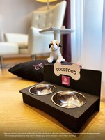 Zona que admite mascotas, con un comedero negro para perro y una figurita de perro pequeño sobre un cojín negro.