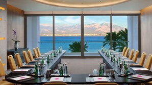 Un salón de conferencias con una larga mesa, sillas y vistas al mar y a las montañas.