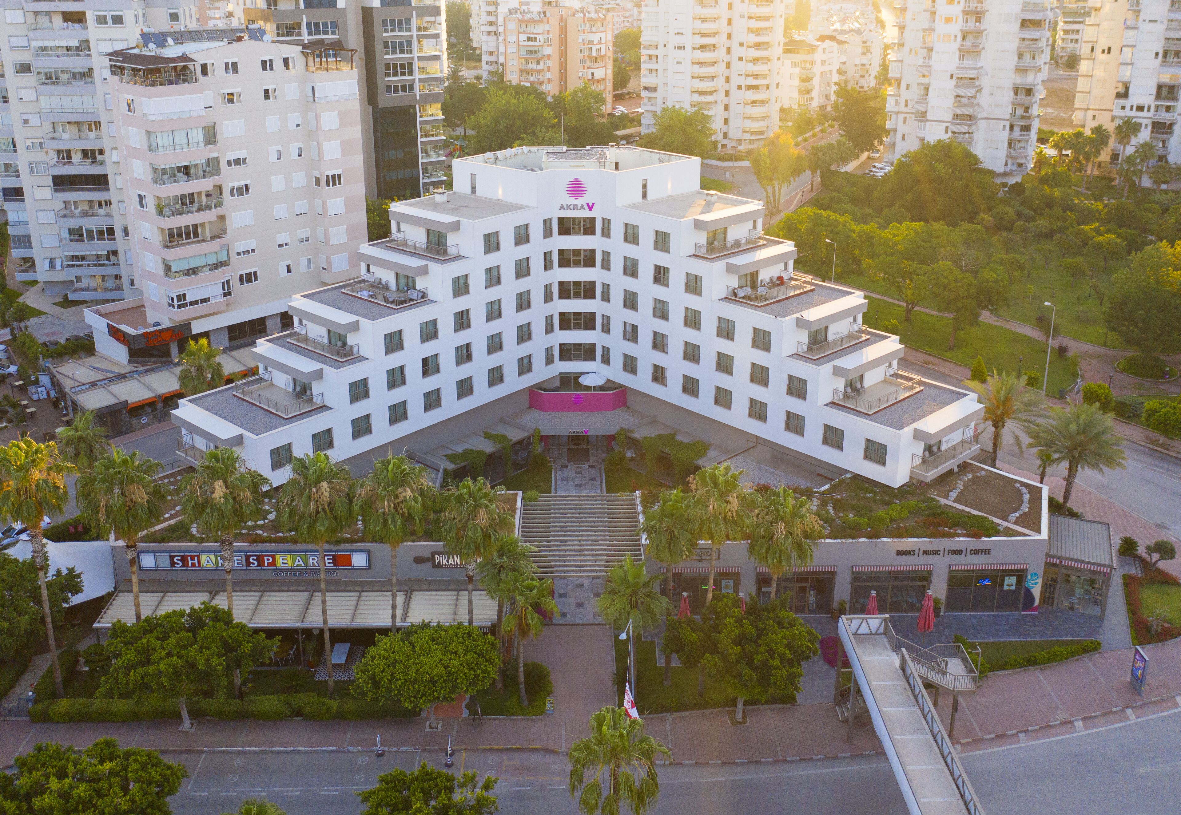 A multi-story hotel with a central atrium, surrounded by palm trees and adjacent to a Shakespeare-themed building.