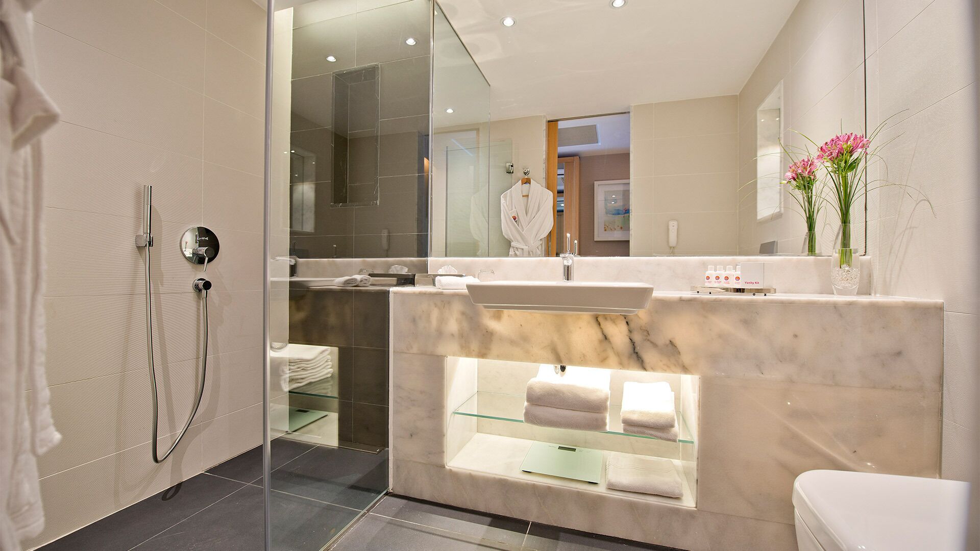 A modern bathroom with a glass-enclosed shower, a marble sink, and a vanity with a glass shelf.