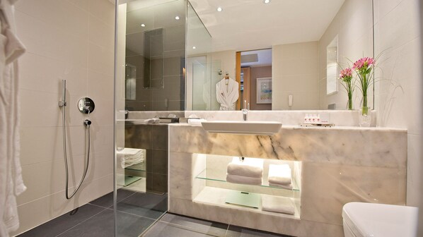 A modern bathroom with a glass-enclosed shower, a marble sink, and a vanity with a glass shelf.