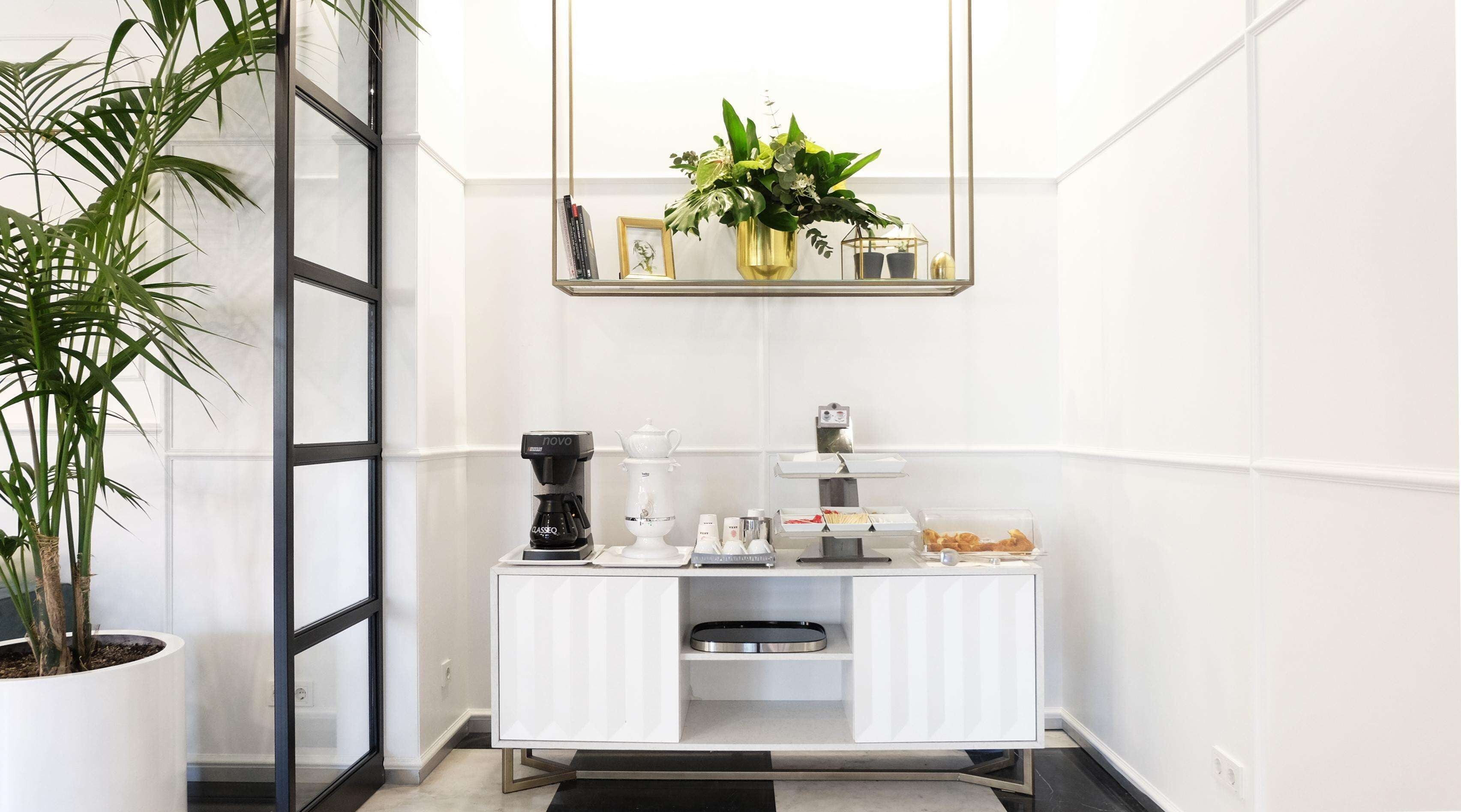 Een moderne kamer met een witte lijst, een koffiehoek, een plant in pot en een spiegel boven het aanrecht.