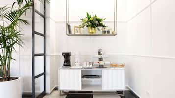 Een moderne kamer met een witte lijst, een koffiehoek, een plant in pot en een spiegel boven het aanrecht.