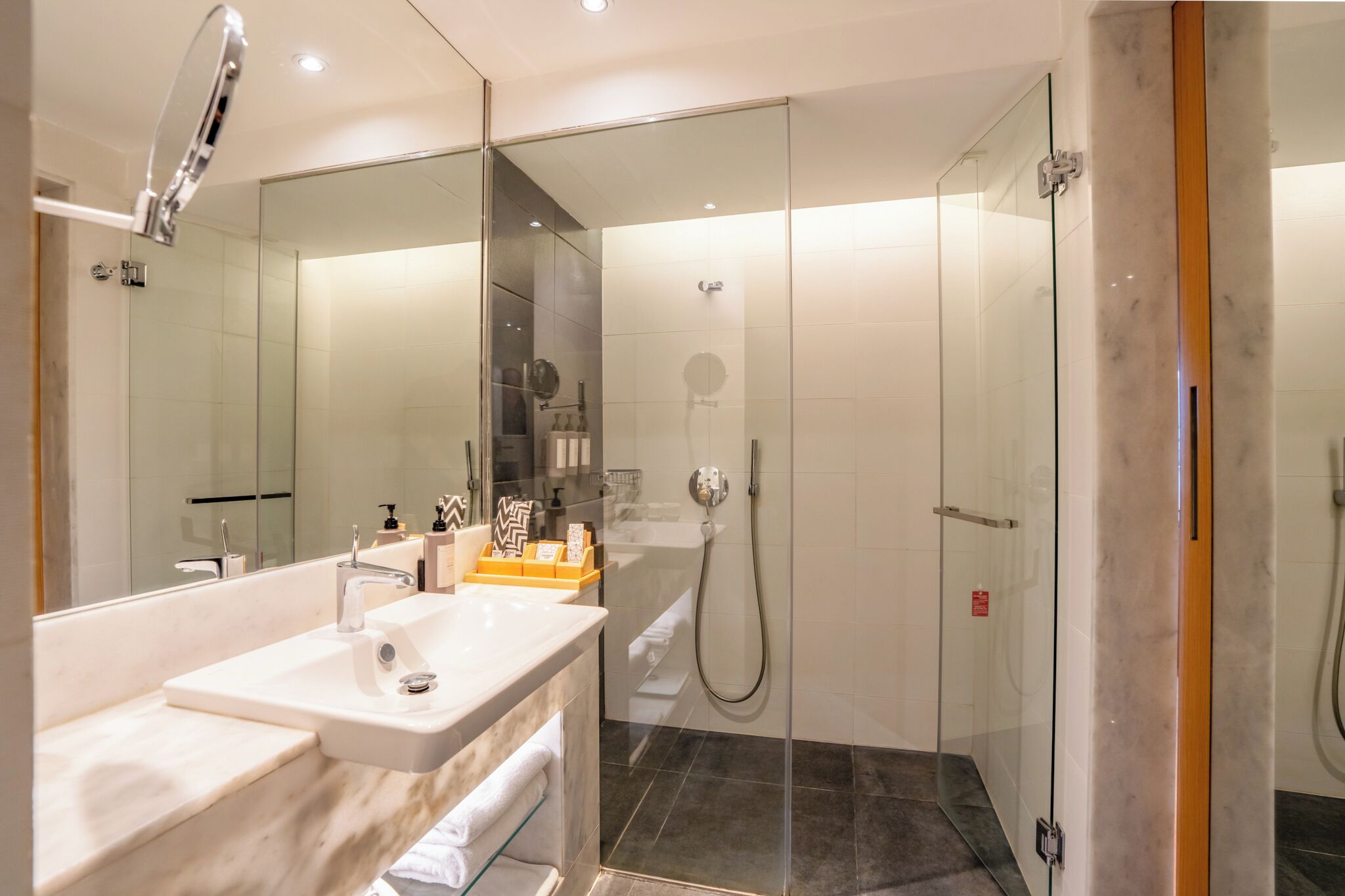 A modern bathroom with a glass-enclosed shower, a large mirror, and a vanity with a sink and towel rack.