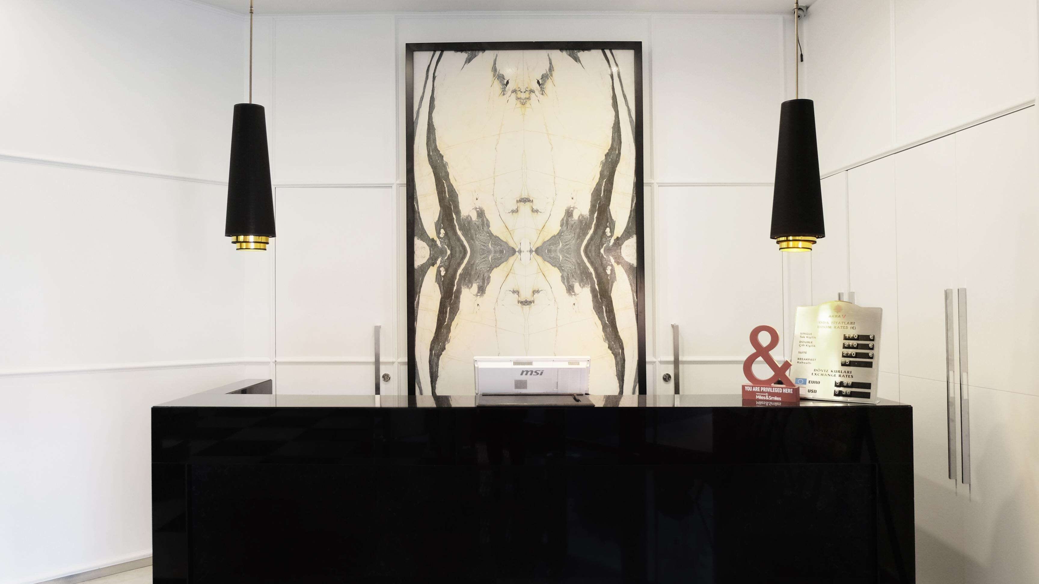 Un mostrador de recepción con superficie negra, dos lámparas colgantes, una pared con diseño simétrico y un cartel con tarifas.