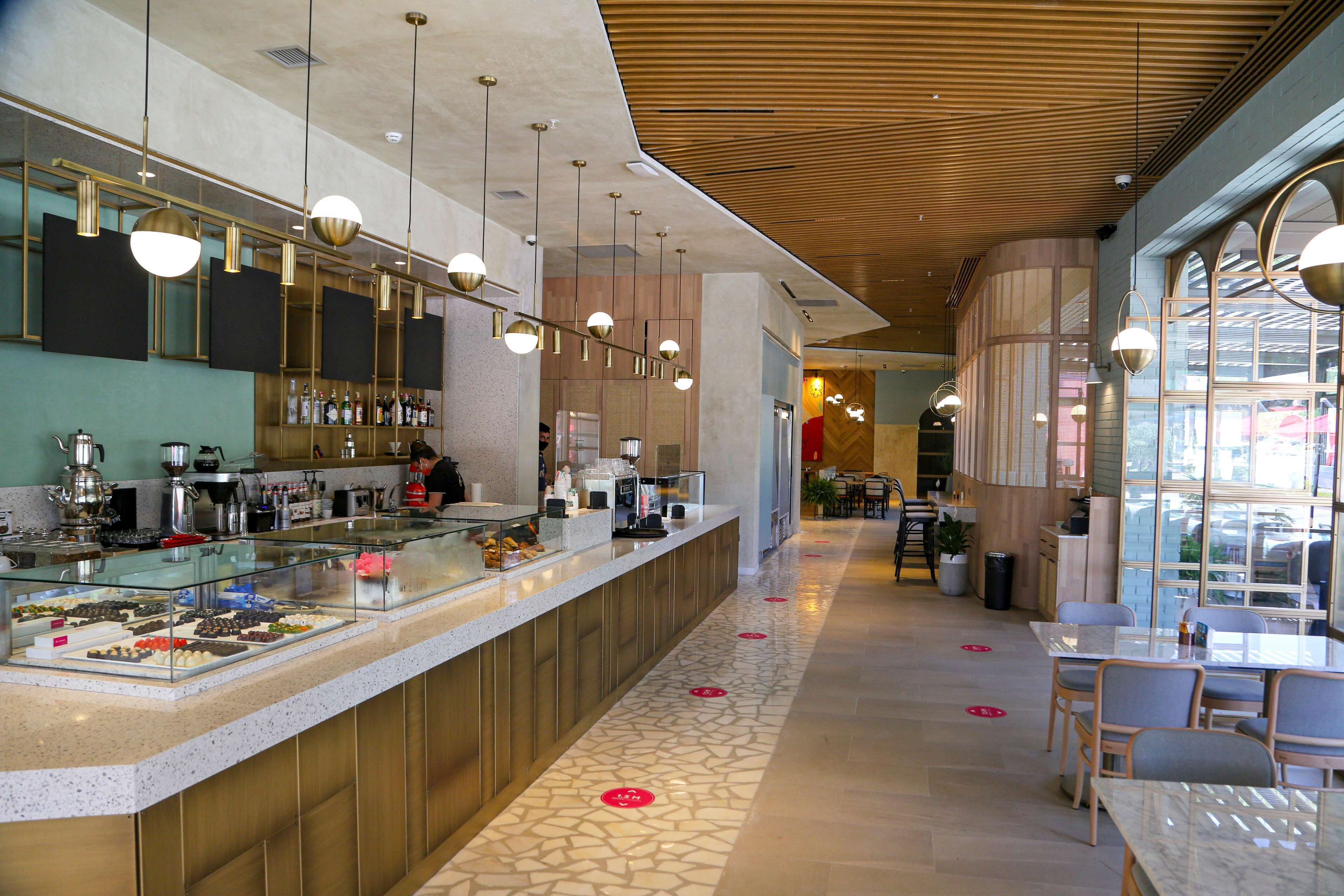 Una cafetería moderna con un mostrador de vidrio que exhibe pasteles, techo de madera y zona de estar con mesas y sillas.