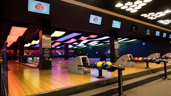 Una bolera con múltiples pistas, bolas de bolos y pantallas publicitarias.