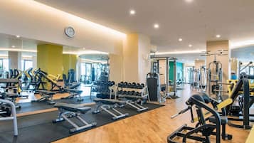 A modern gym with various exercise equipment, a large mirror, and a clock on the wall.