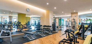 A modern gym with various exercise equipment, a large mirror, and a clock on the wall.