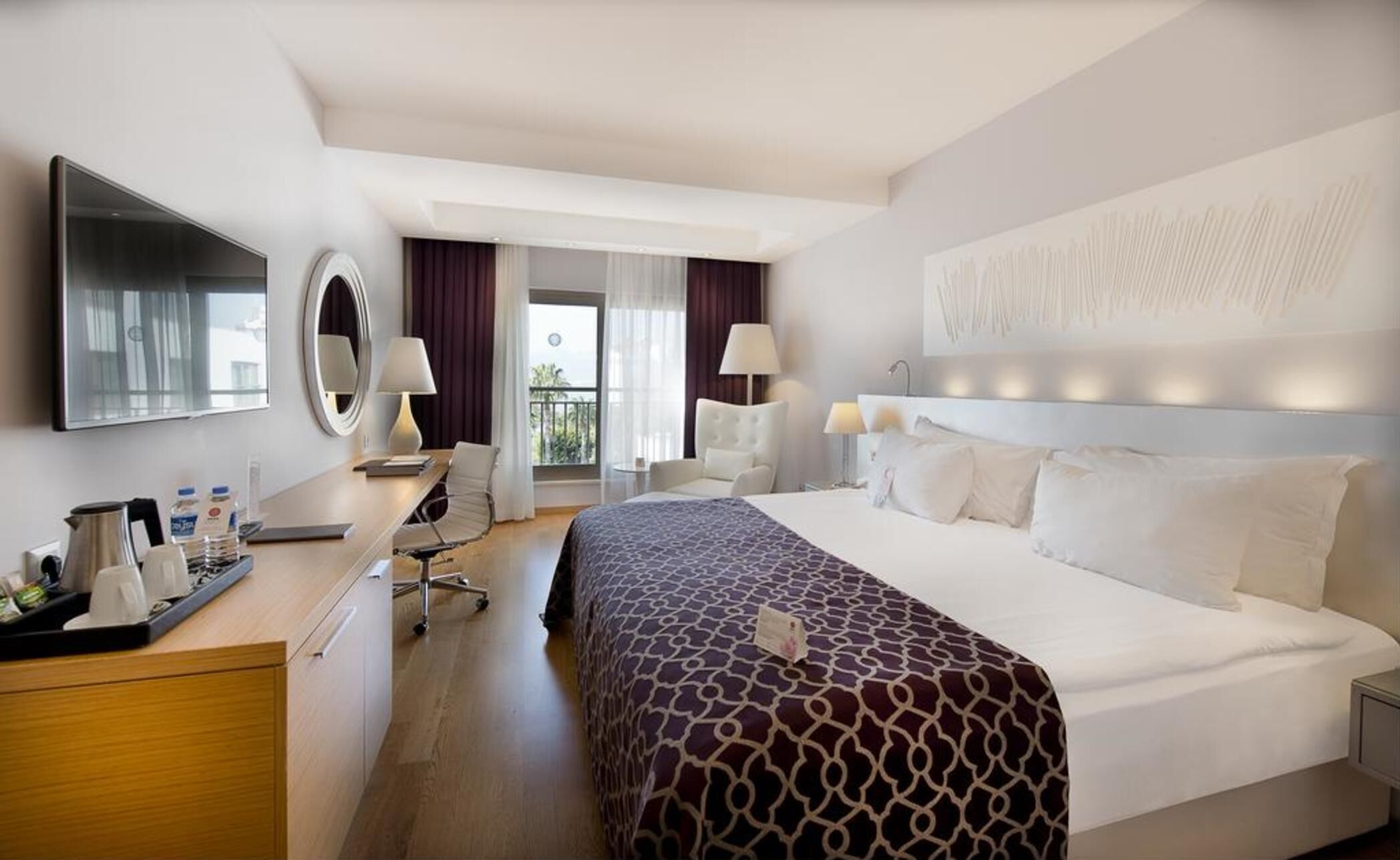 Habitación de hotel con cama, escritorio, silla, televisor y vistas al balcón.