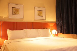Una habitación de hotel con una cama, dos cuadros en la pared, una lámpara y una cortina oscura.