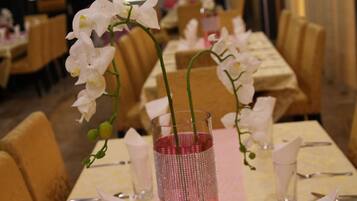 Uma mesa de jantar com um vaso rosa e orquídeas brancas, rodeada por cadeiras e louças bem organizadas.