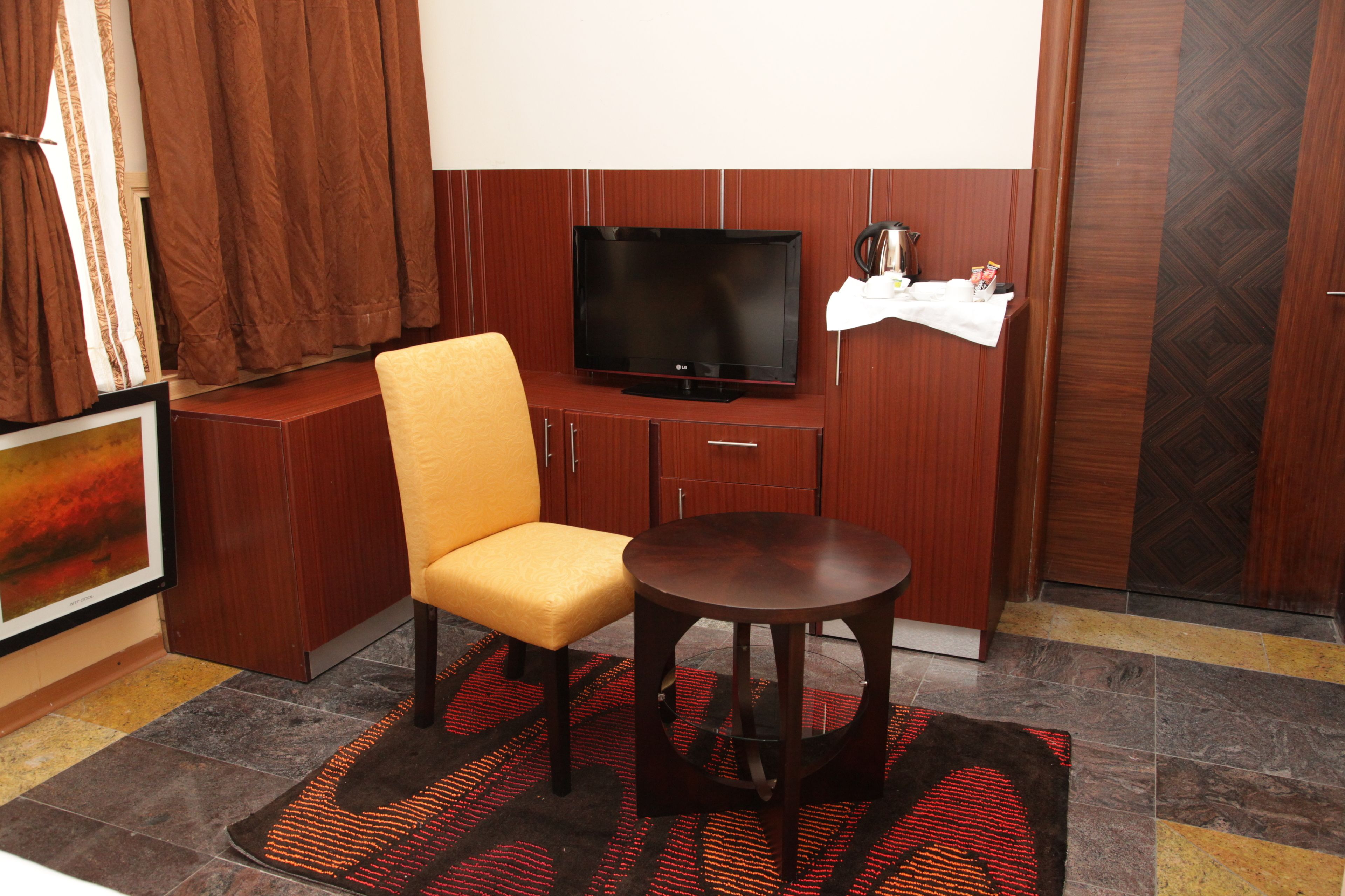 A hotel room with a television, a yellow chair, a small round table, and a patterned rug.