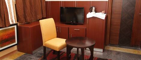 A hotel room with a television, a yellow chair, a small round table, and a patterned rug.