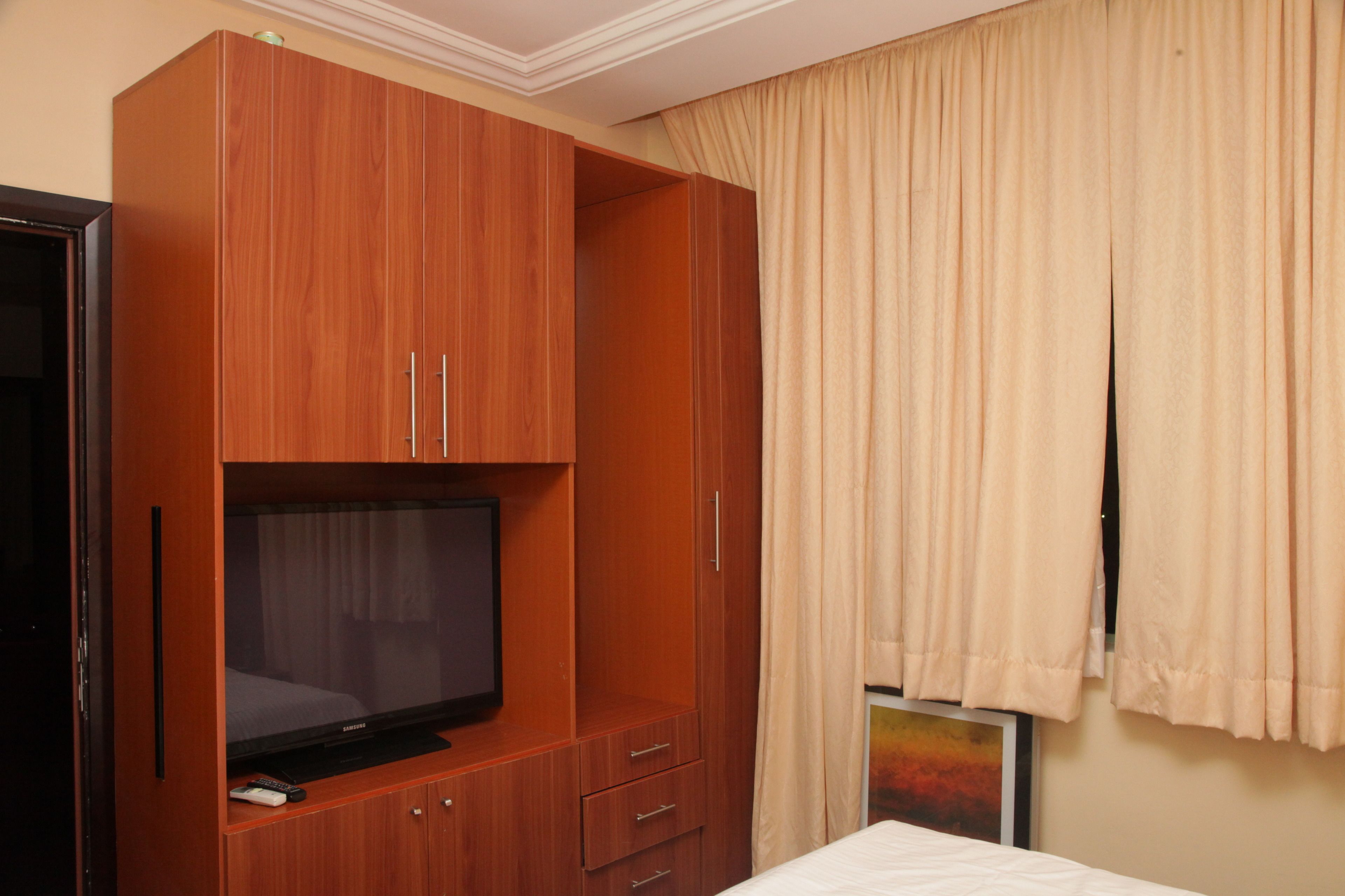 A hotel room with a wooden wardrobe, a television, and a bed.