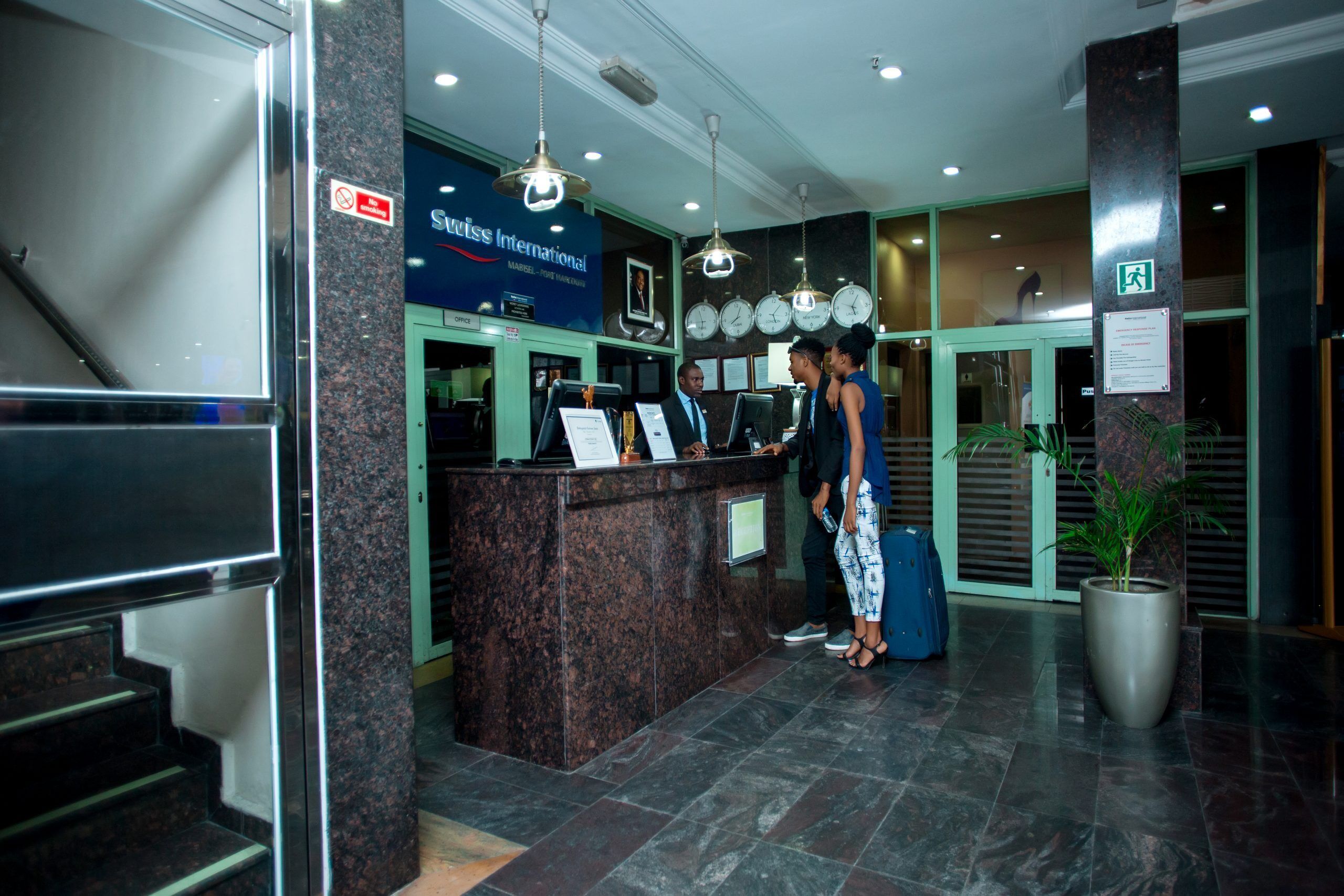 A reception desk with a sign for Swiss International, a clock, and a potted plant.