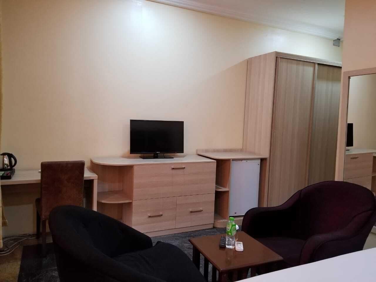 Une chambre d’hôtel équipée d’une télévision, d’un bureau, d’une chaise, d’une armoire et d’une petite table avec une bouteille.