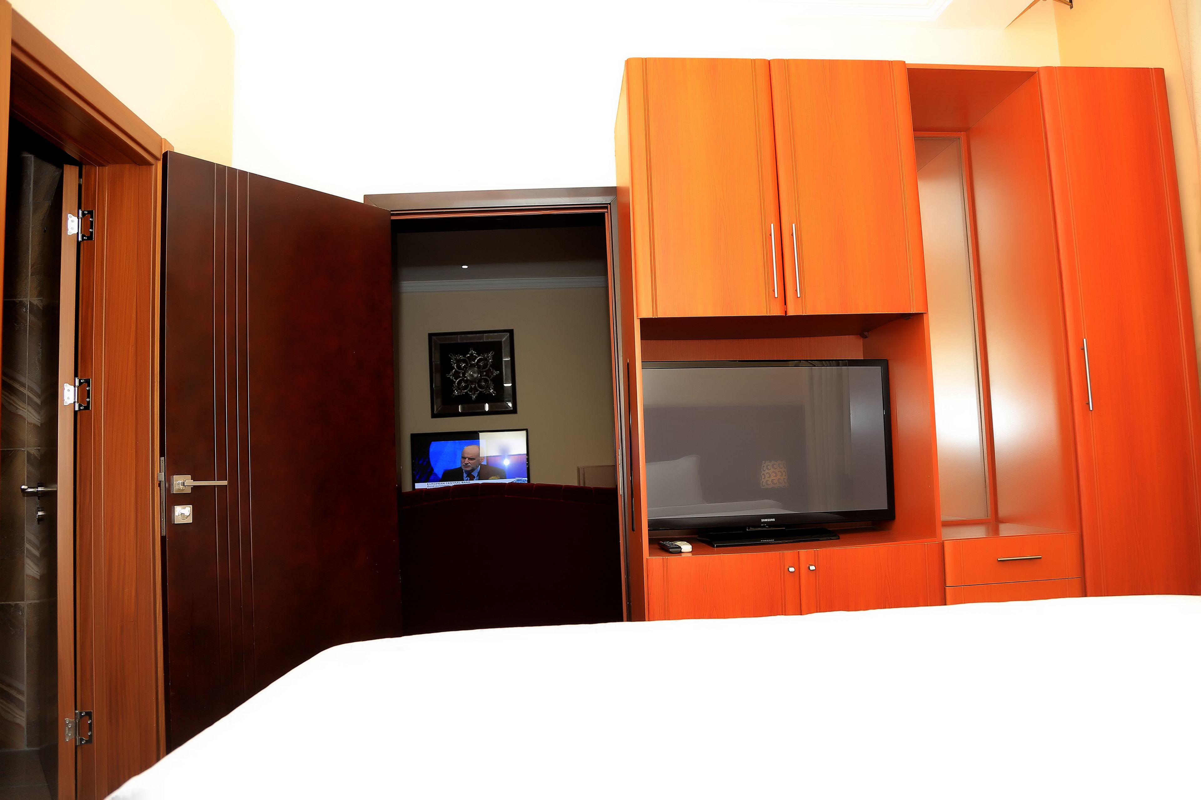 A hotel room with a bed, a television, a desk with a computer, and a wardrobe.
