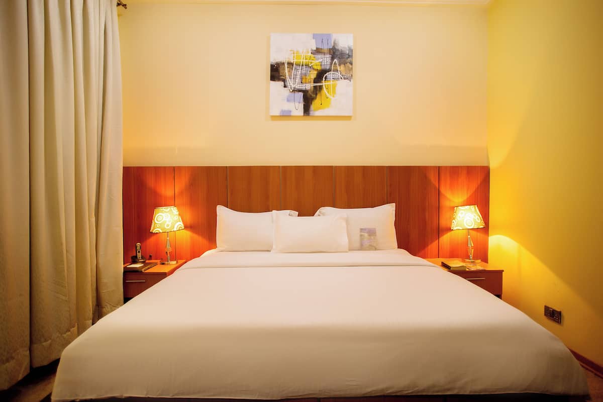 Een hotelkamer met een groot bed, twee bedlampen, een houten hoofdbord en een schilderij aan de muur.