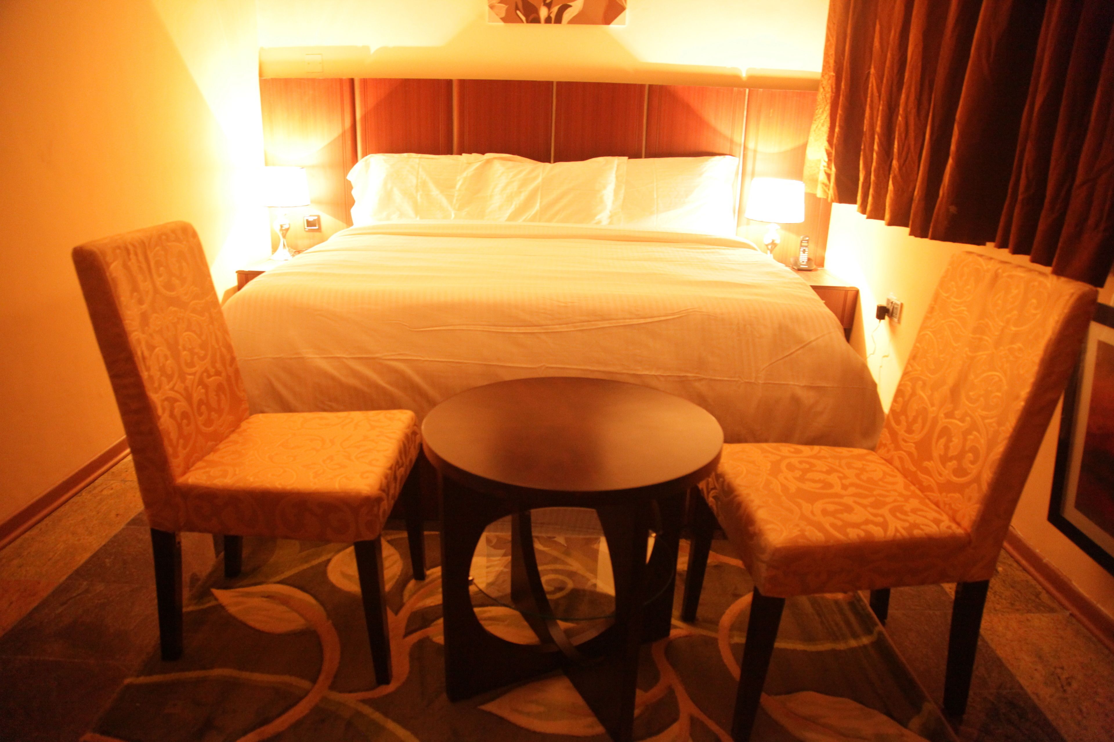 Une chambre d’hôtel comprenant un lit, deux fauteuils, une petite table ronde et une table de chevet avec une lampe.