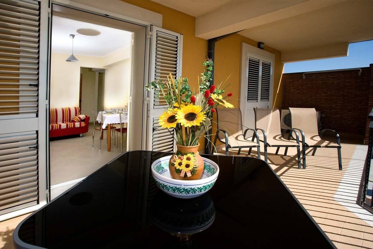 Zona pranzo con tavolo, sedie e un vaso con girasoli.