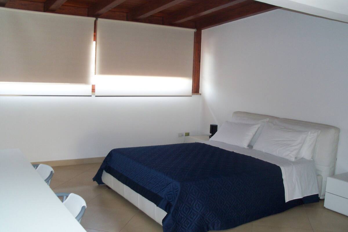 Una camera da letto con un letto, un comodino e una finestra con persiane.