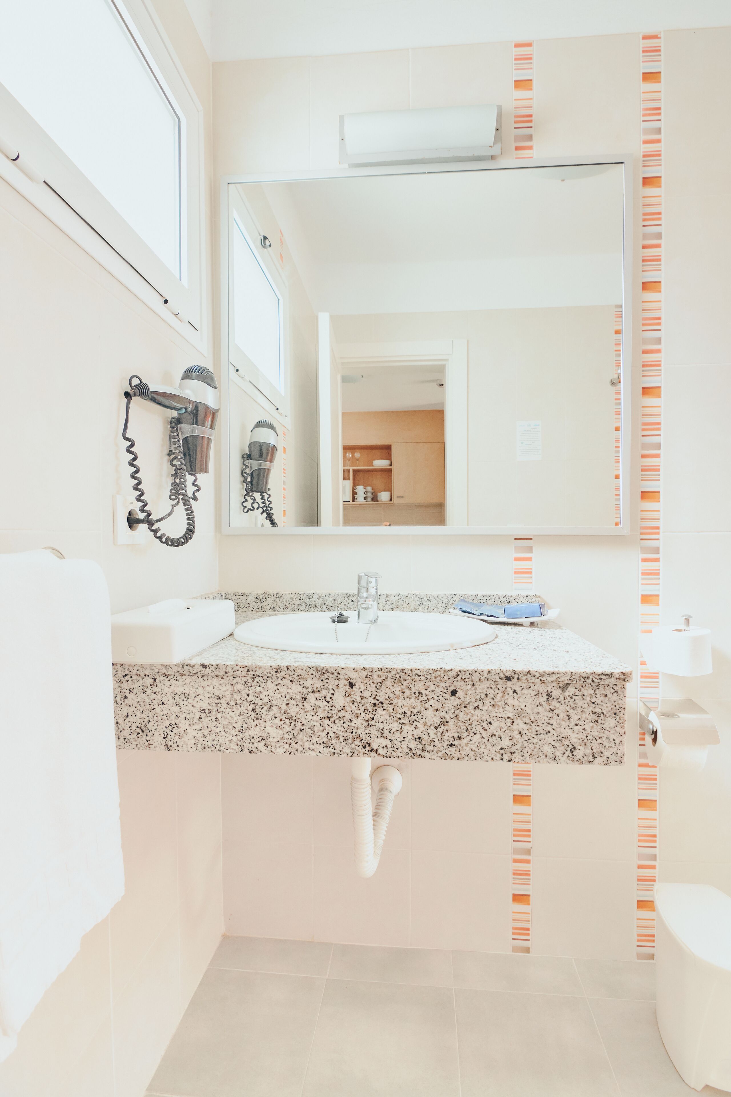 A bathroom with a sink, mirror, hairdryer, and toilet.