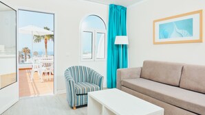 A living room with a beige sofa, a striped armchair, a white coffee table, a window with teal curtains, and a framed picture on the wall. - Gloria Izaro Club Hotel (Tías)