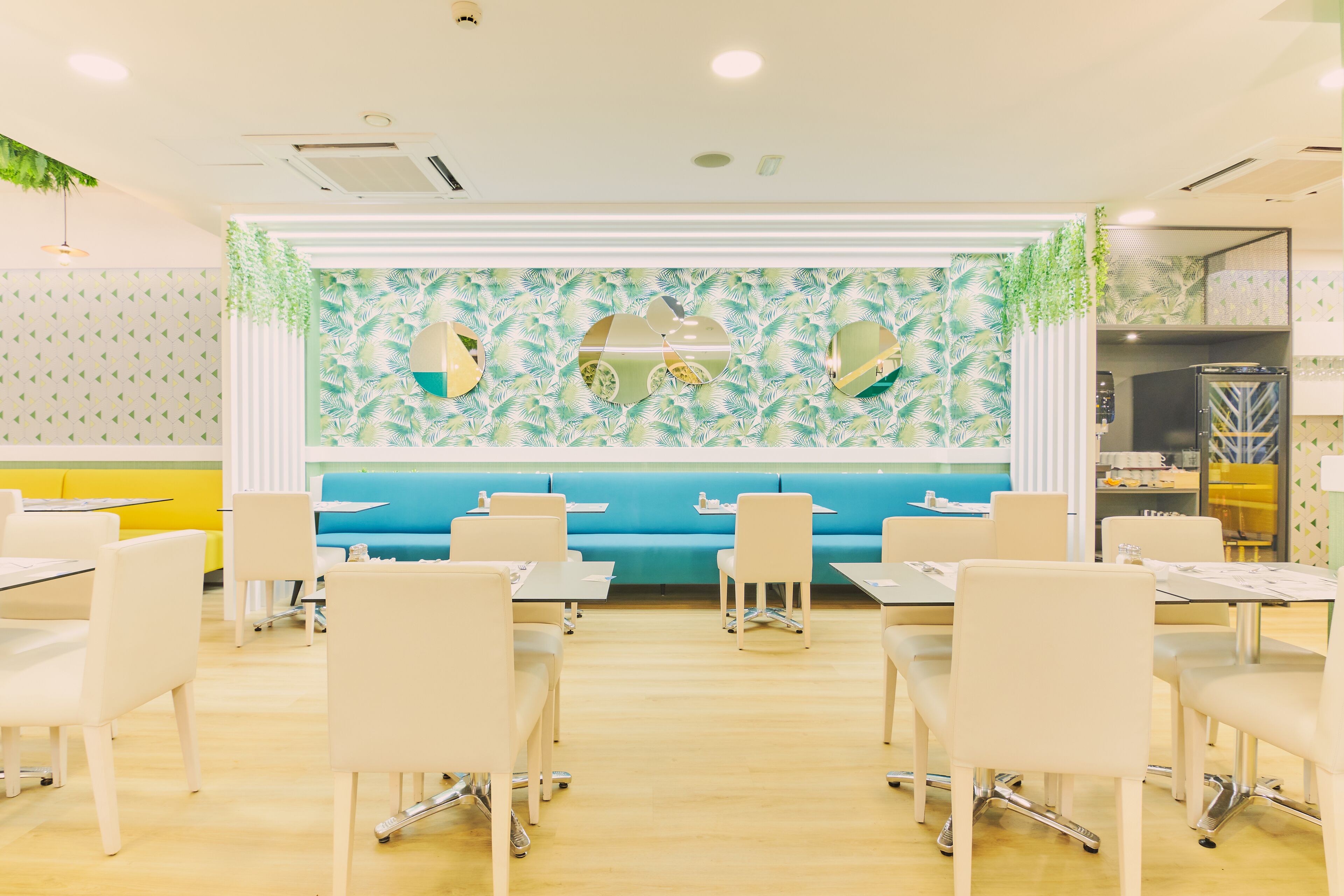 A dining area with tables and chairs, a blue booth, and a wall with decorative mirrors and greenery.